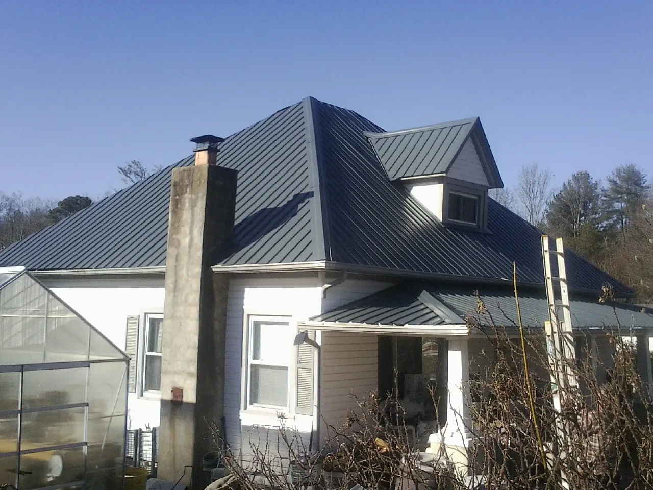 Dark blue standing seam metal roof on a white farmhouse with dormer — Slate & Tile Roof Repair by Roofing Brothers in Oldenburg