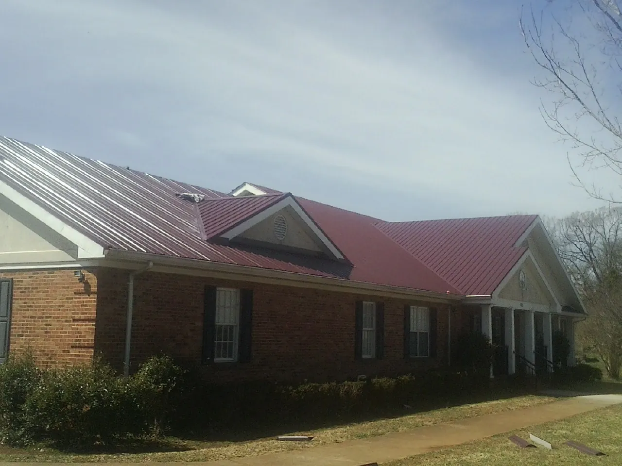 Red metal roof with gabled entries on a long brick building, from a Hail Damage Roof Repair job in Oldenburg