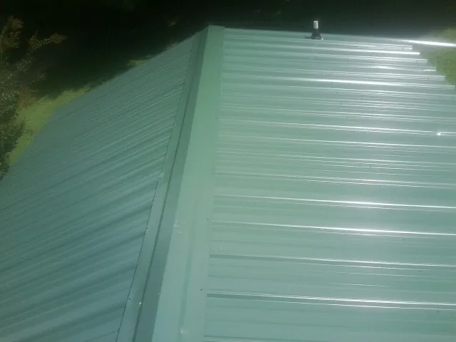 New green metal panels meeting at the ridge of a roof — Flat Roof Repair work by our crew in Oldenburg