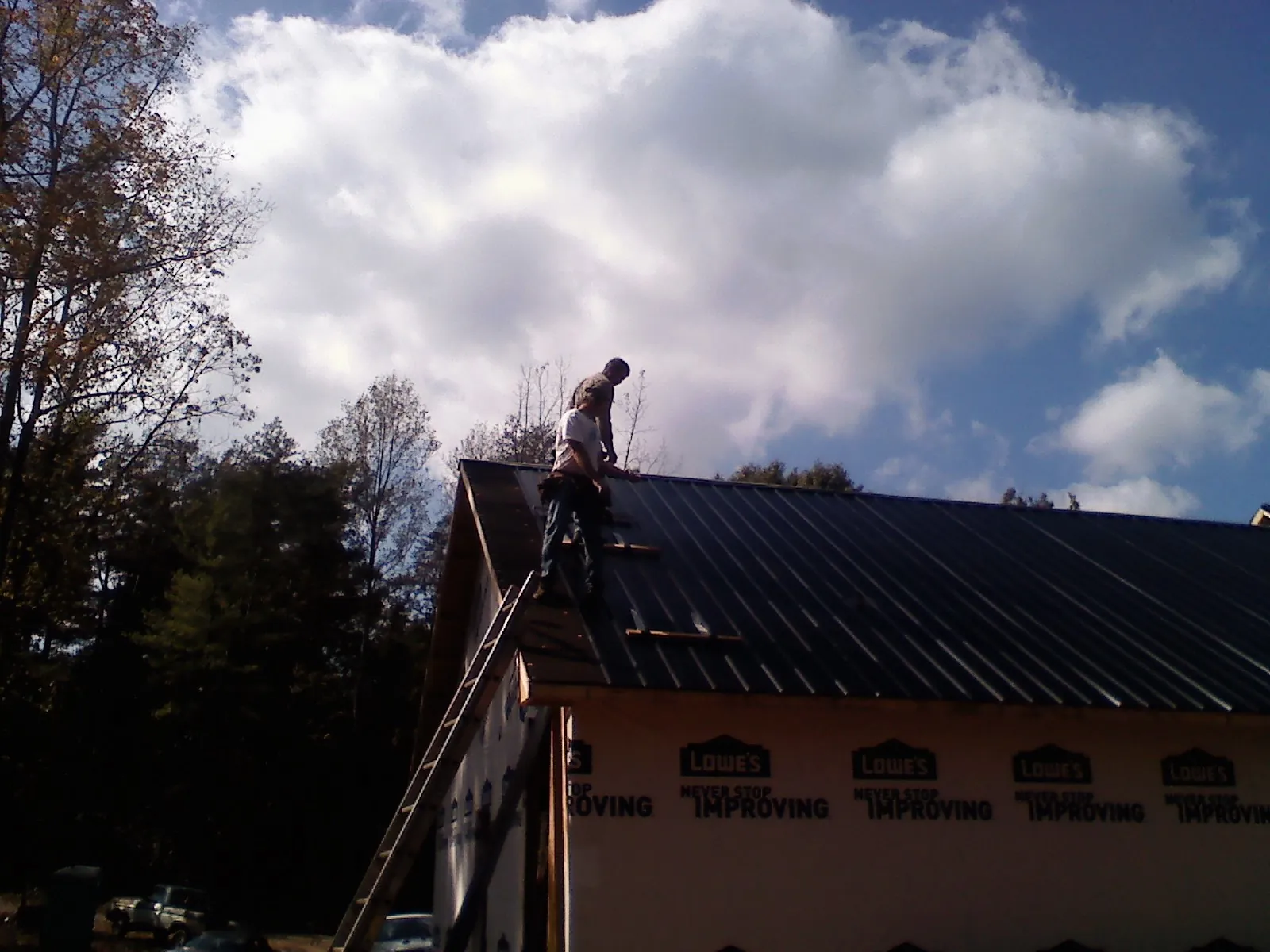 Roofer fastening dark metal panels high against a cloudy sky, from a Roof Inspection job in Oldenburg