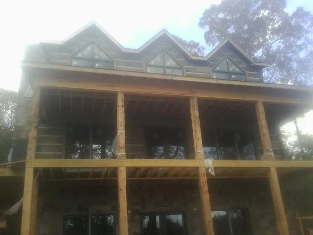 Dormers and porch framing on a large log home under construction — Roof Coating work by our crew in Oldenburg