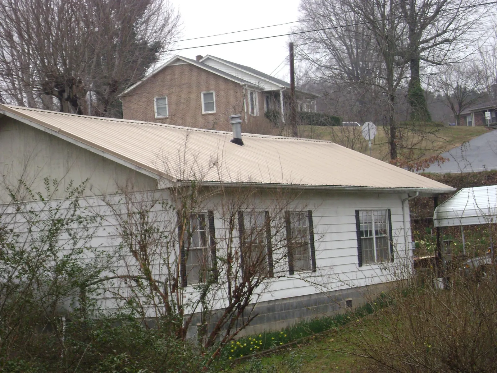Tan metal roof on a white sided house set into a hillside — Commercial Roofing by Roofing Brothers in Oldenburg